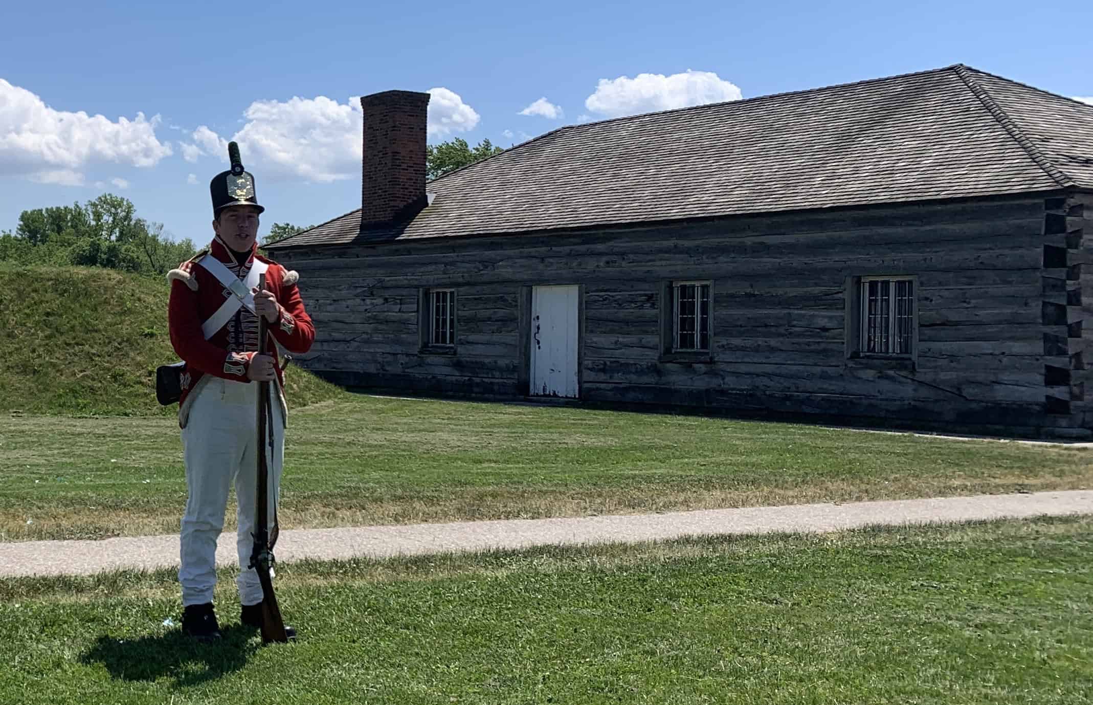 A staff member at Fort George is dressed in 1812 period British army uniform costume, speaking before a musket demonstration.