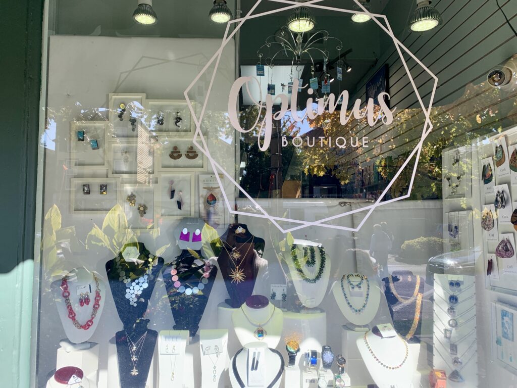 A window display of jewelry through glass that has the Optimus logo on it.