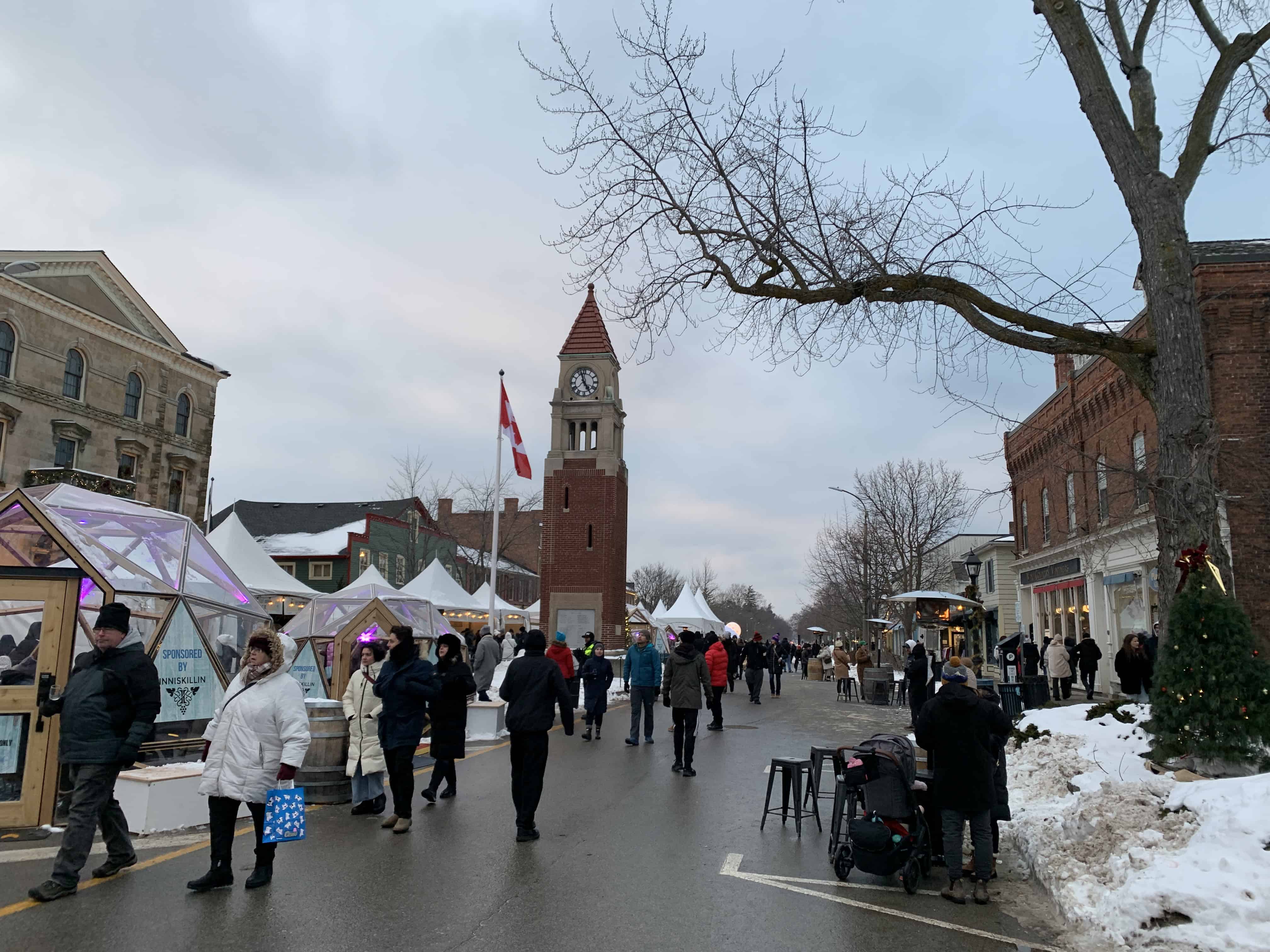 Queen Street in Niagara-on-the-Lake bustling with visitors during the 2025 Icewine Festival. The street features charming historic architecture, lighted igloo-like structures, and festival-goers enjoying winter attractions.