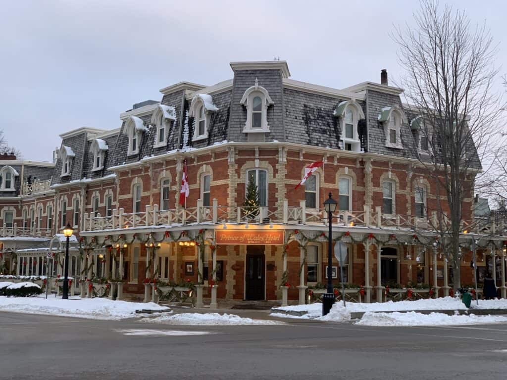 The historic Prince of Wales Hotel in Niagara-on-the-Lake, adorned with festive garlands and flags during the winter season. Snow-covered streets enhance the charm of this iconic building.