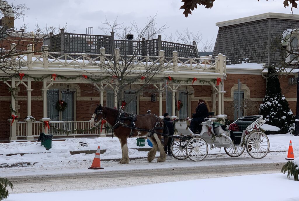 A horse-drawn carriage waits in front of the historic Prince of Wales Hotel in Niagara-on-the-Lake in the winter. The snowy street and festive decorations create a quintessential holiday scene.