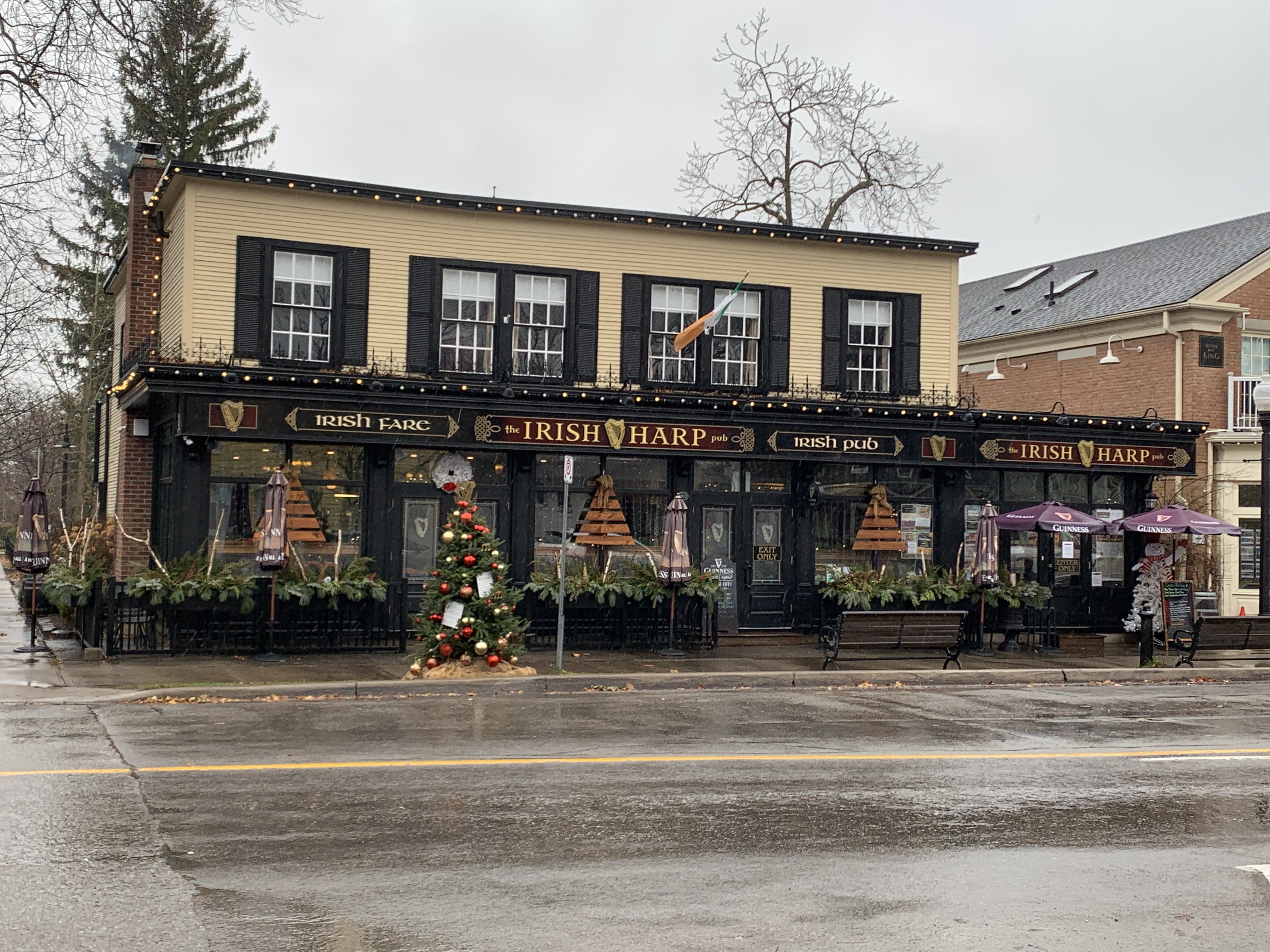 The Irish Harp Pub in downtown Niagara-on-the-Lake in winter, decorated with festive garlands and lights. The cozy pub offers a picturesque view with its traditional Irish charm on a cold, rainy day.